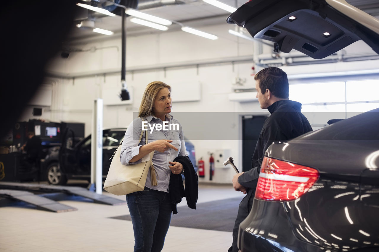Customer discussing with mechanic leaning on car in repair shop