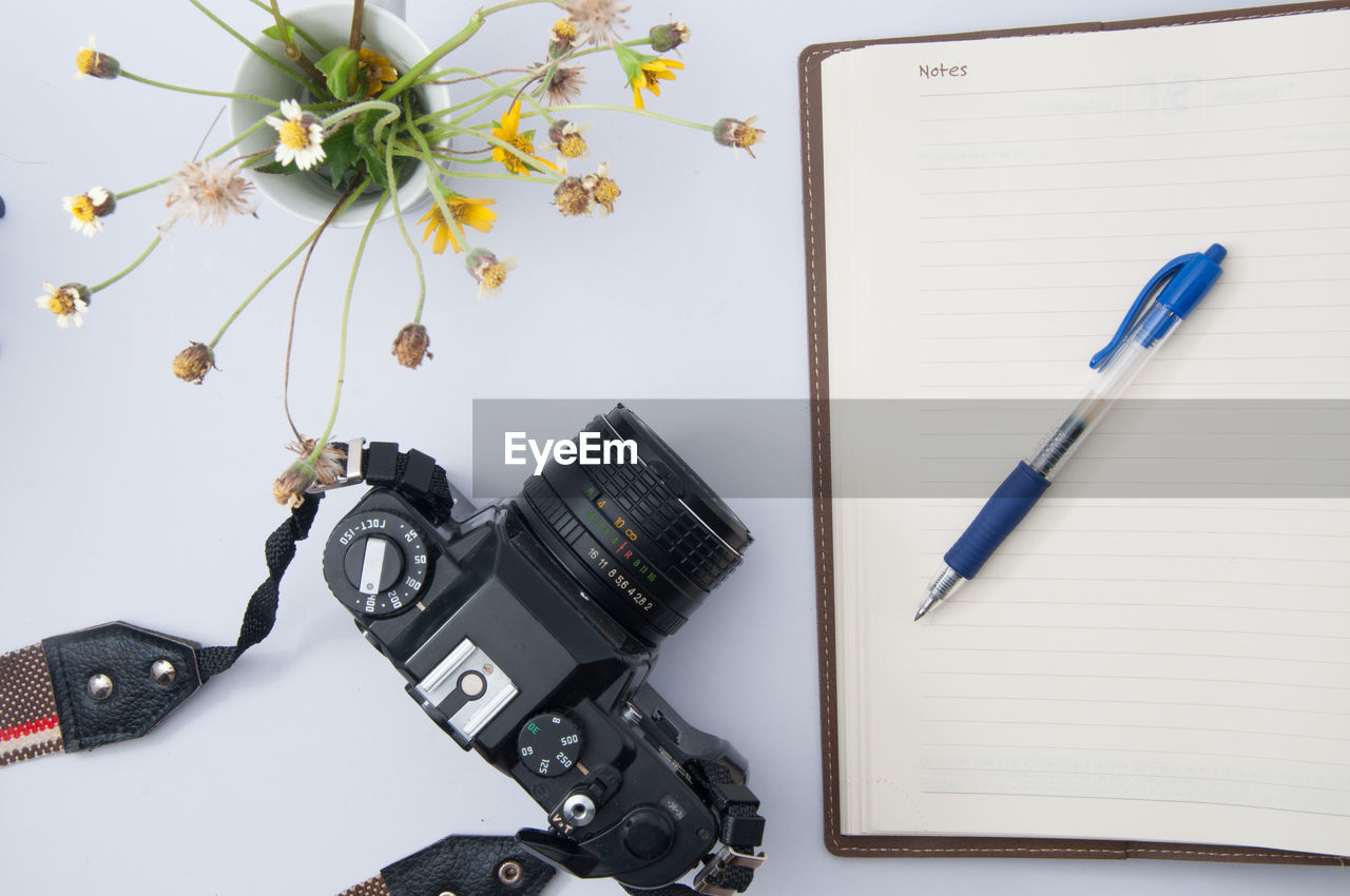 Close-up of camera with flower vase and diary on table