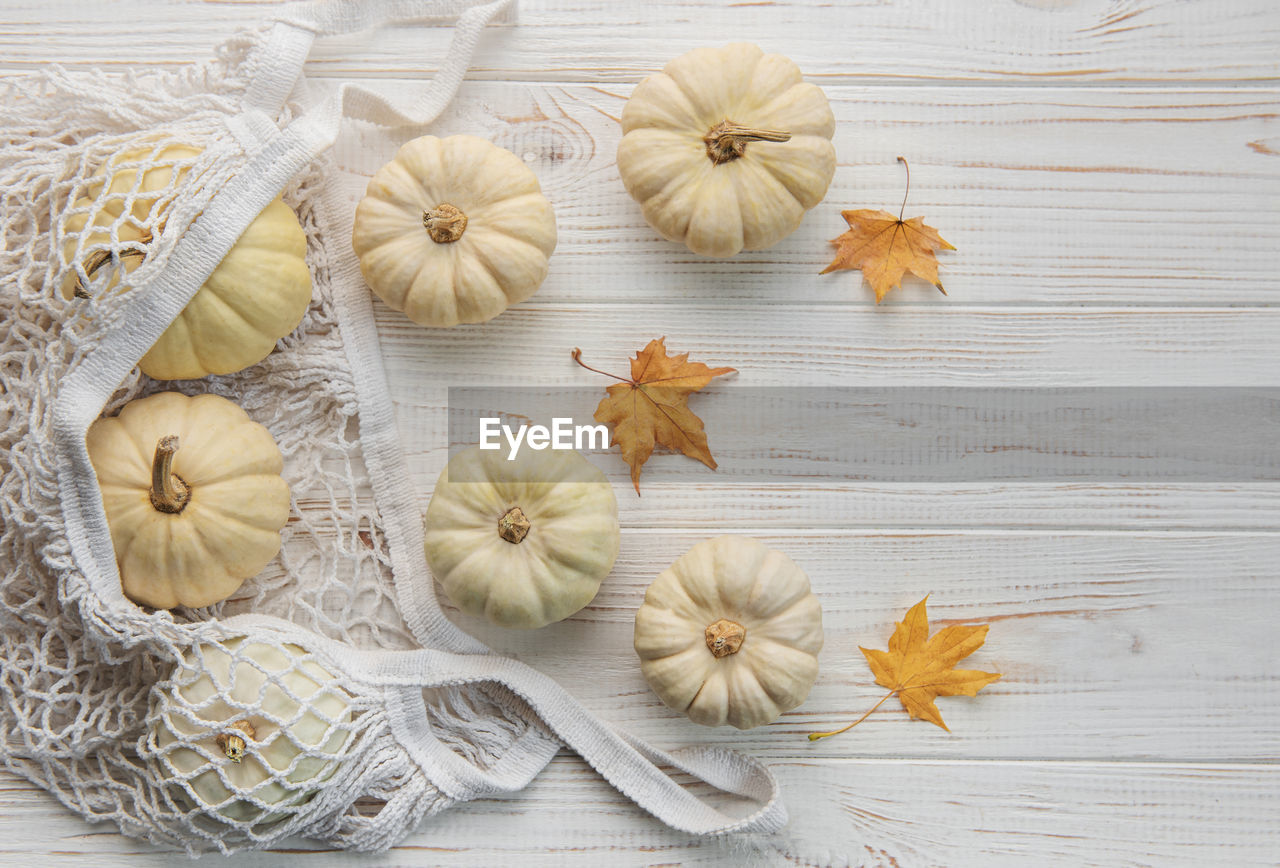 Top view autumn composition with pumpkins in mesh shopping bag on a wooden background