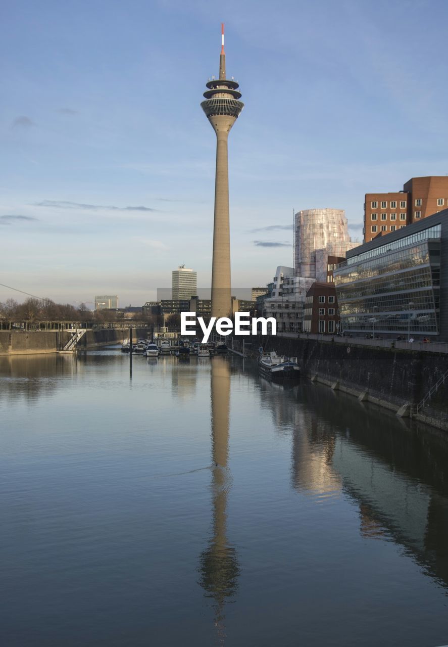 River in front of rheinturm tower in city against sky