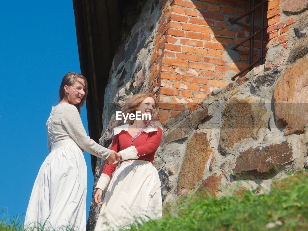 Smiling two women standing against brick wall