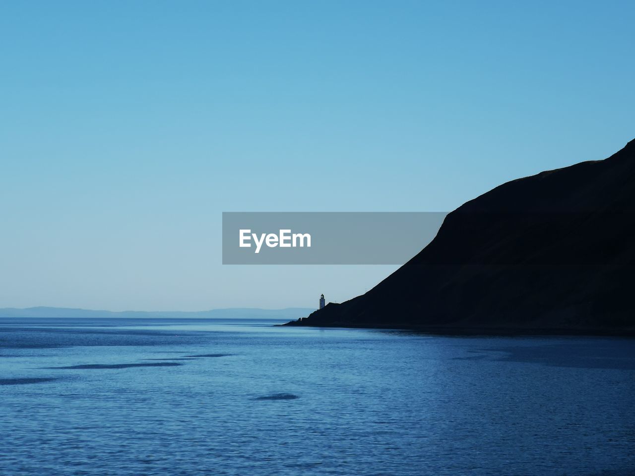 SILHOUETTE MOUNTAIN BY SEA AGAINST CLEAR BLUE SKY