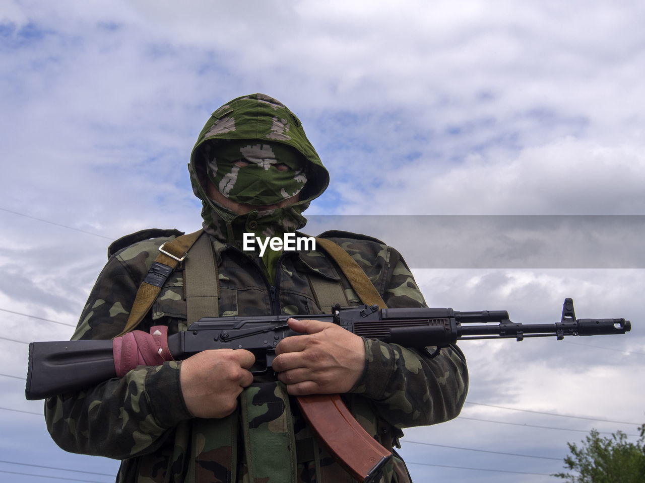 Army soldier holding rifle against cloudy sky