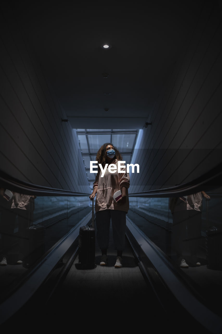 Young woman wearing protective face mask standing on escalator during covid-19