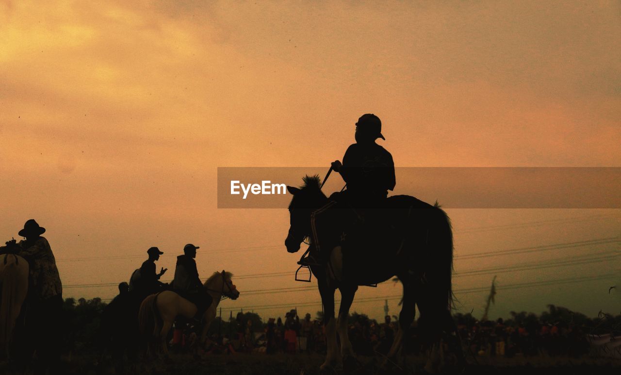 Silhouette people riding horses against sky during sunset