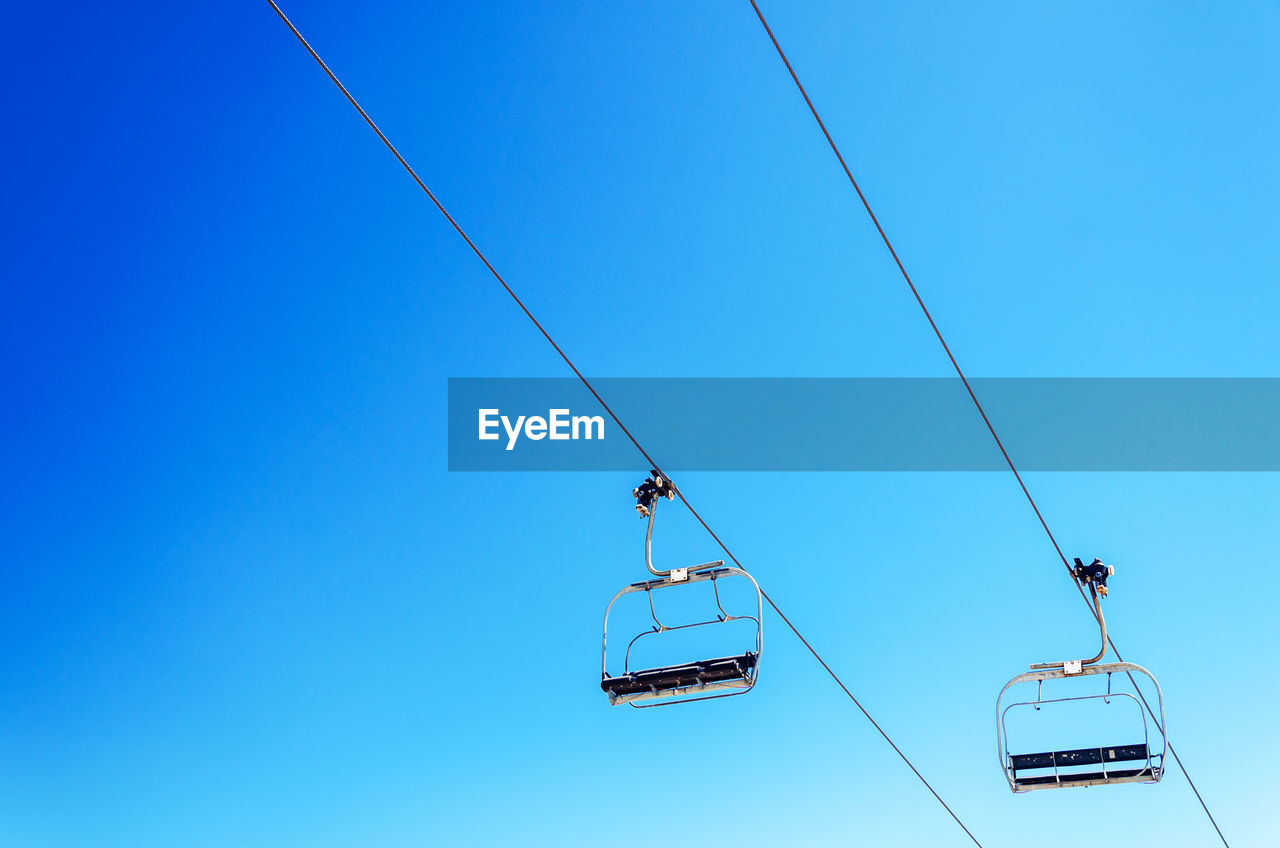 Low angle view of overhead cable cars against clear blue sky