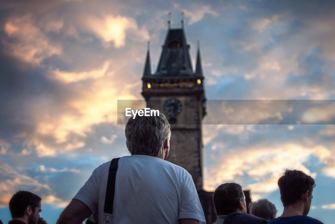Rear view of people by astronomical clock tower against cloudy sky during sunset