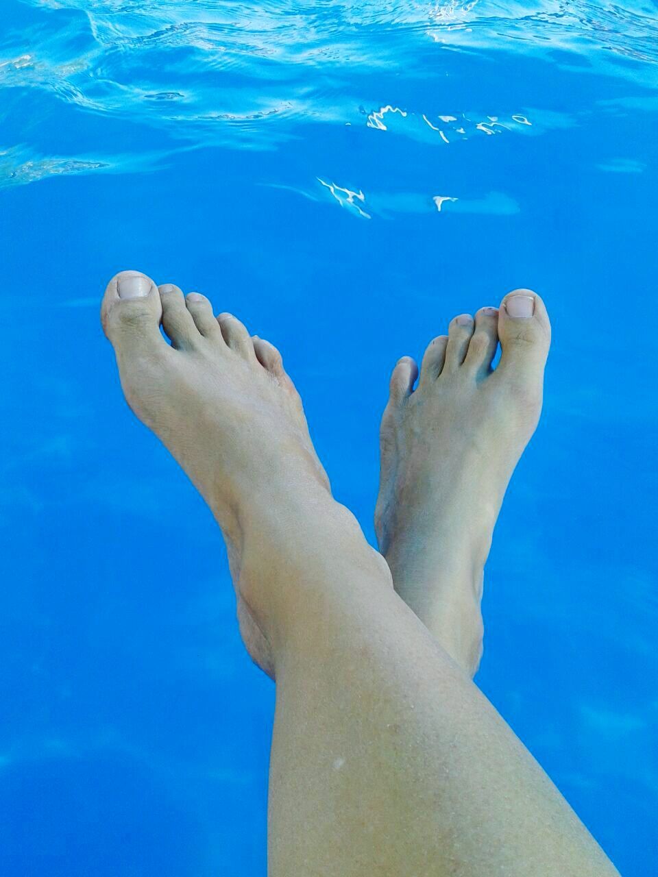 Low section of woman dangling feet over water