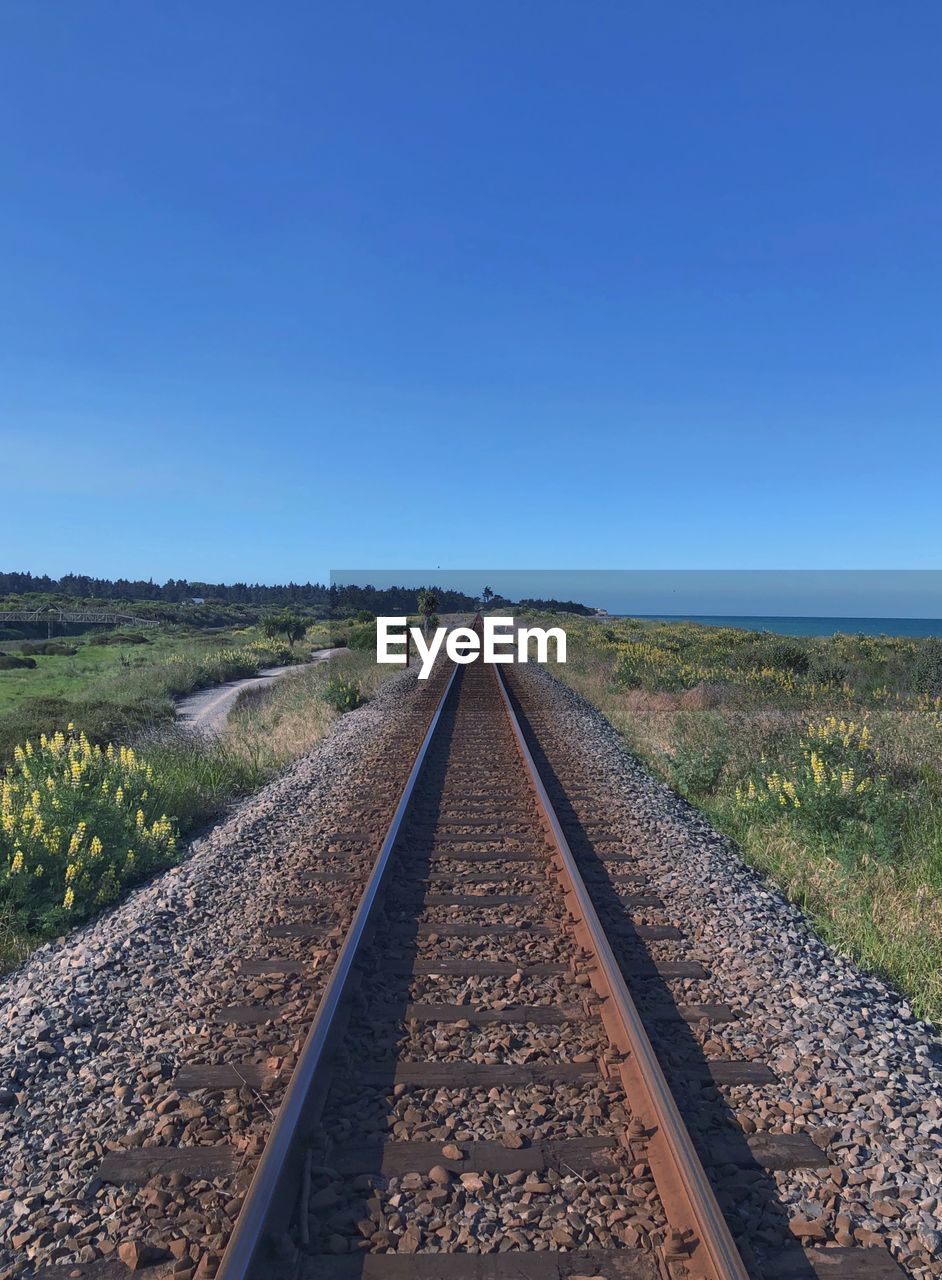 Empty railroad tracks against clear blue sky