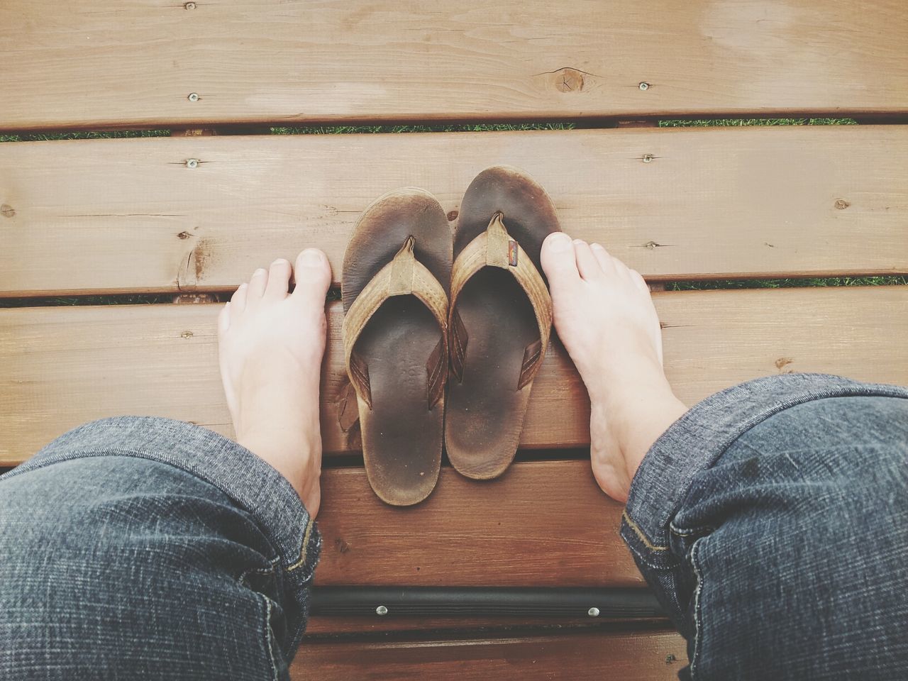 Low section of person sitting with flip-flop on boardwalk