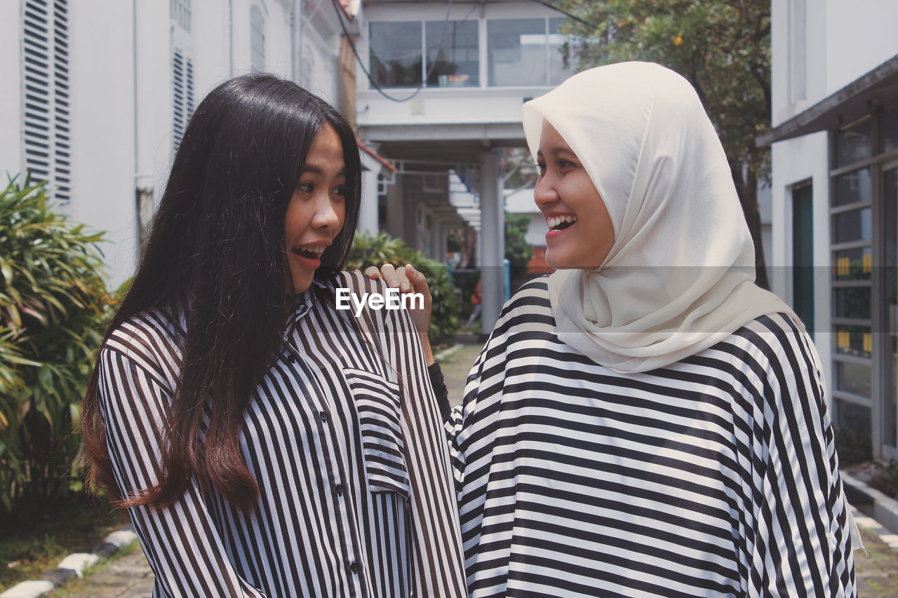 Happy female friends talking while standing against buildings