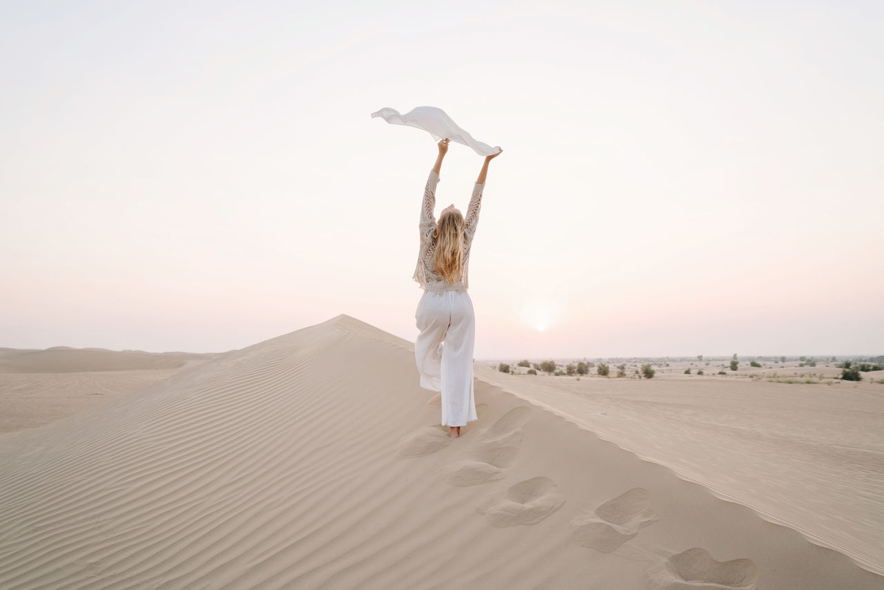 Woman holding scarf in the sand dune in desert