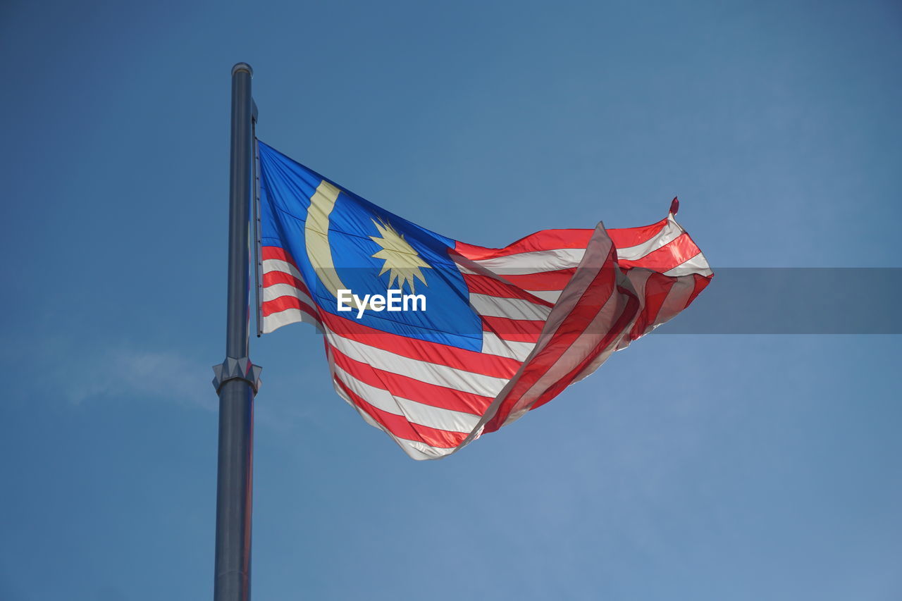 Low angle view of malaysian flag against blue sky