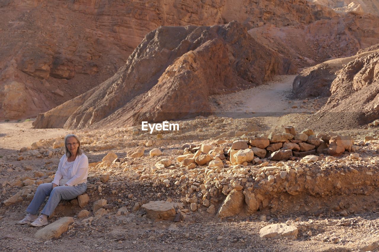 Senior woman sitting on rock against mountains at desert