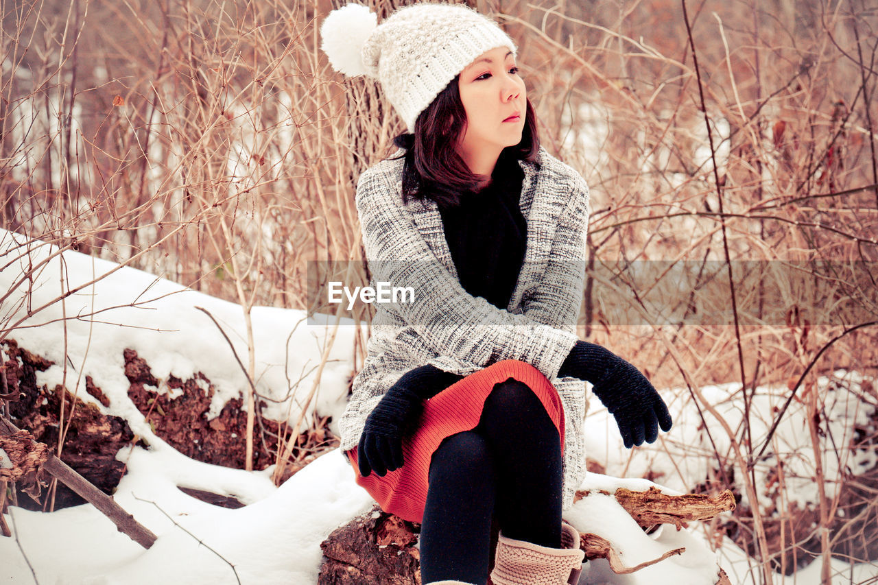Young woman sitting on snow covered tree during winter