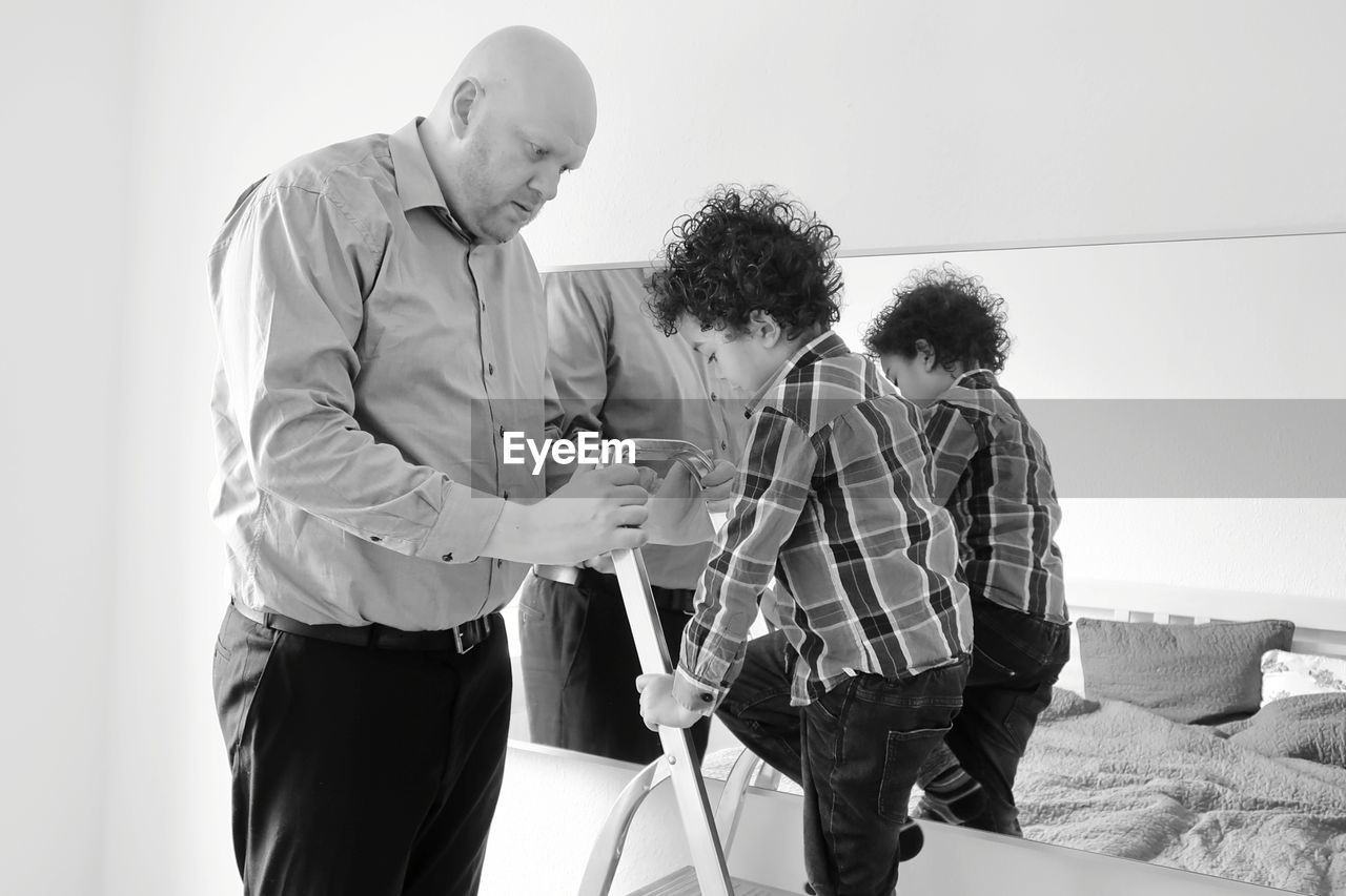 Boy climbing on ladder held by father at home