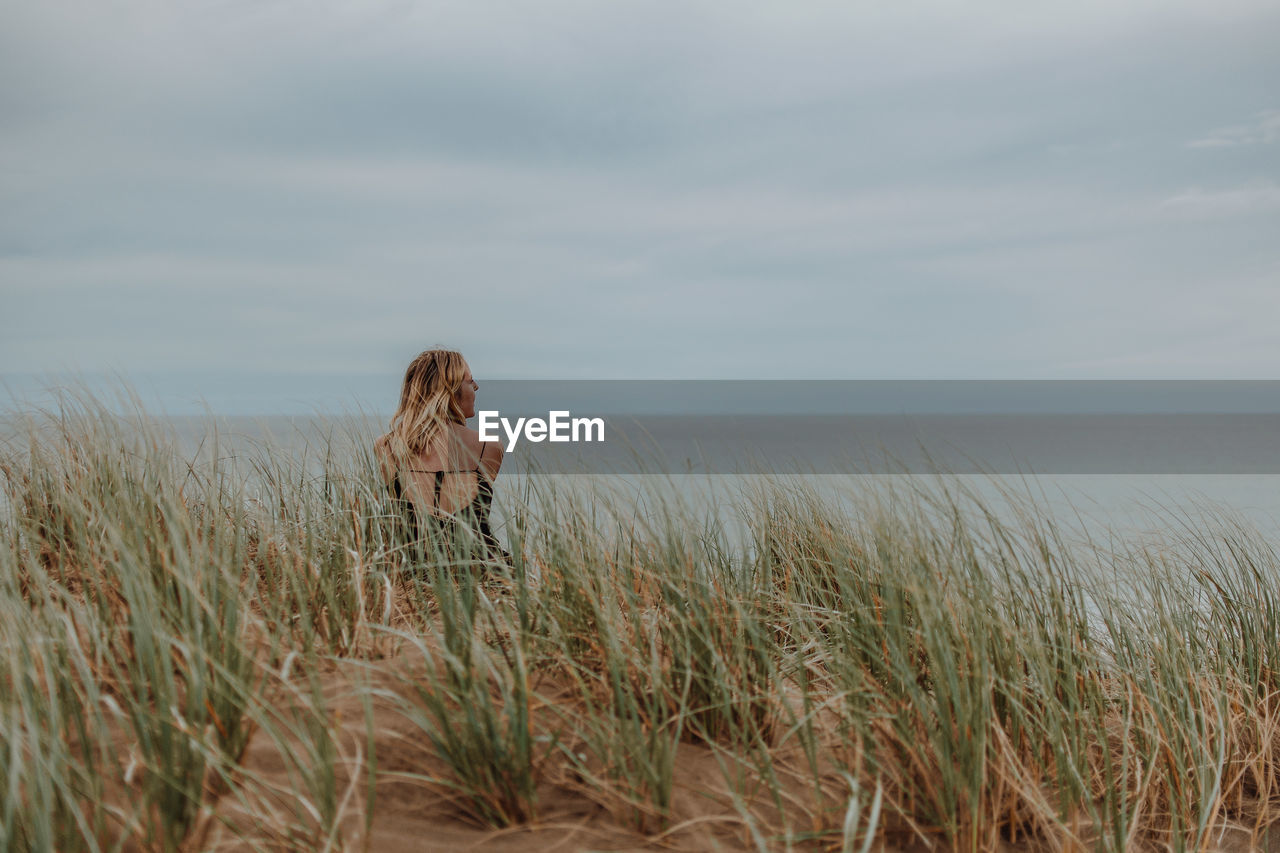 Woman standing on grass by sea against sky