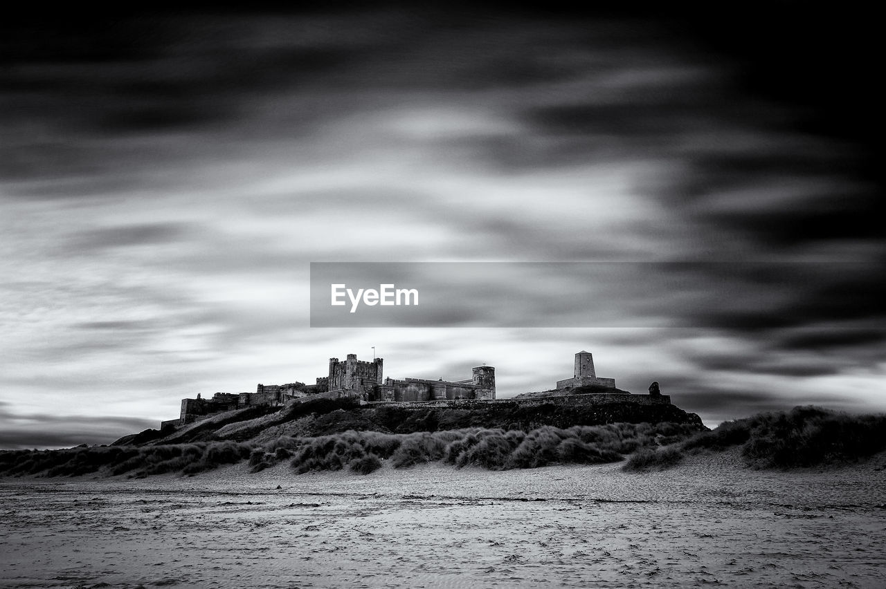 Bamburgh castle by sea against cloudy sky