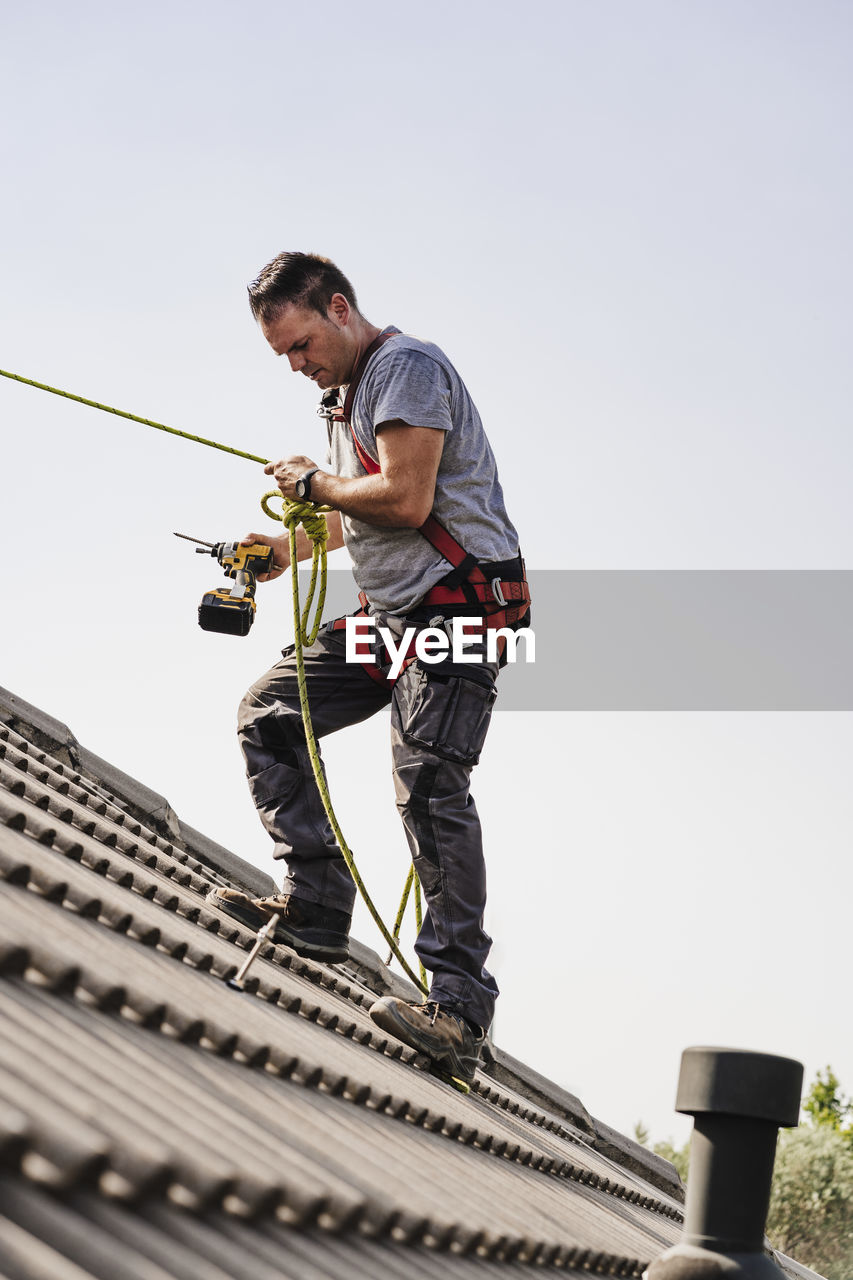 Craftsman with power tool holding rope standing on roof