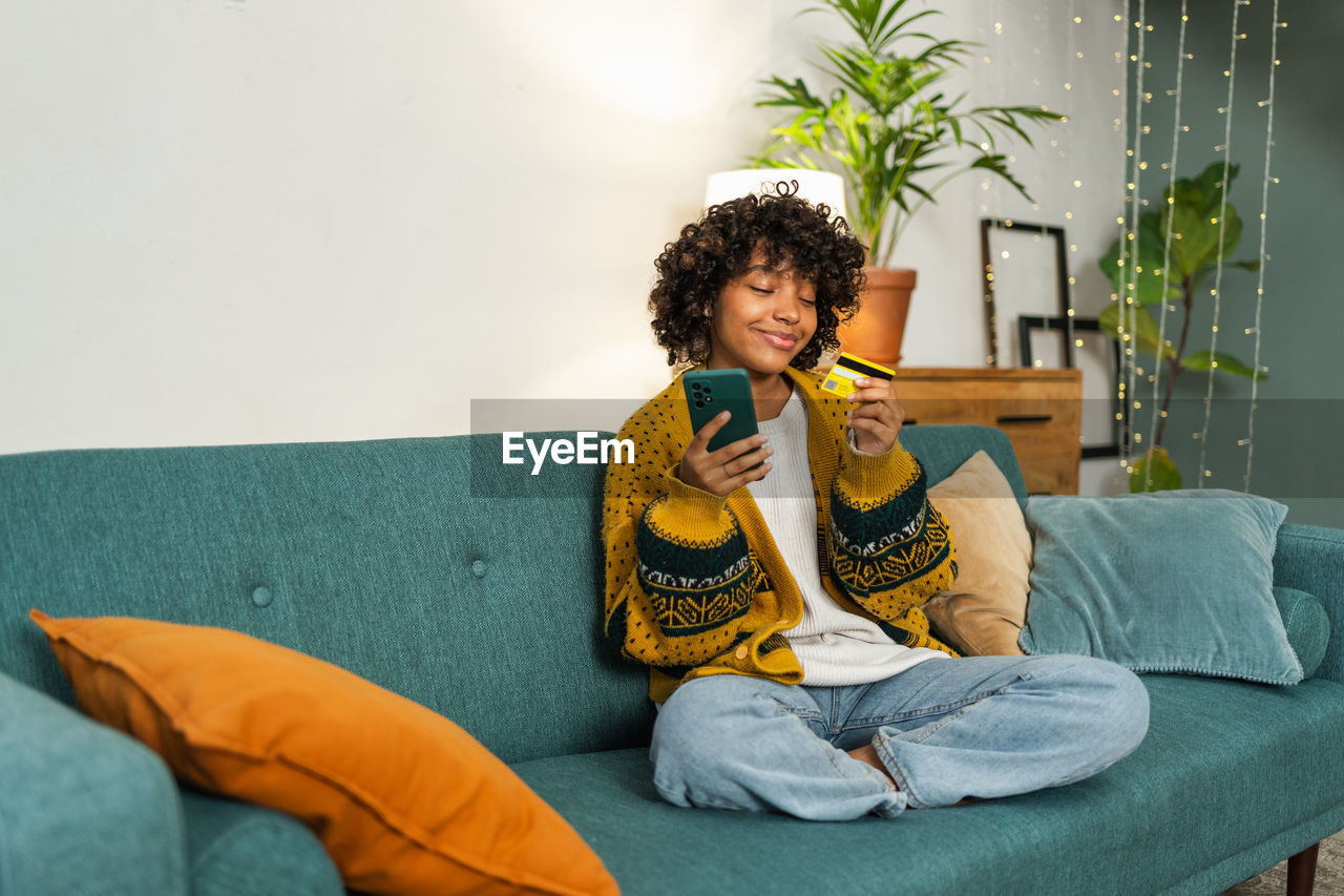 portrait of young woman using mobile phone while sitting on sofa at home