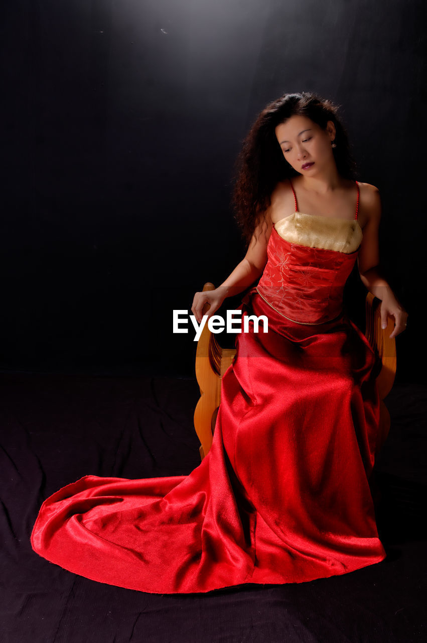 Full length of woman sitting on chair against black background