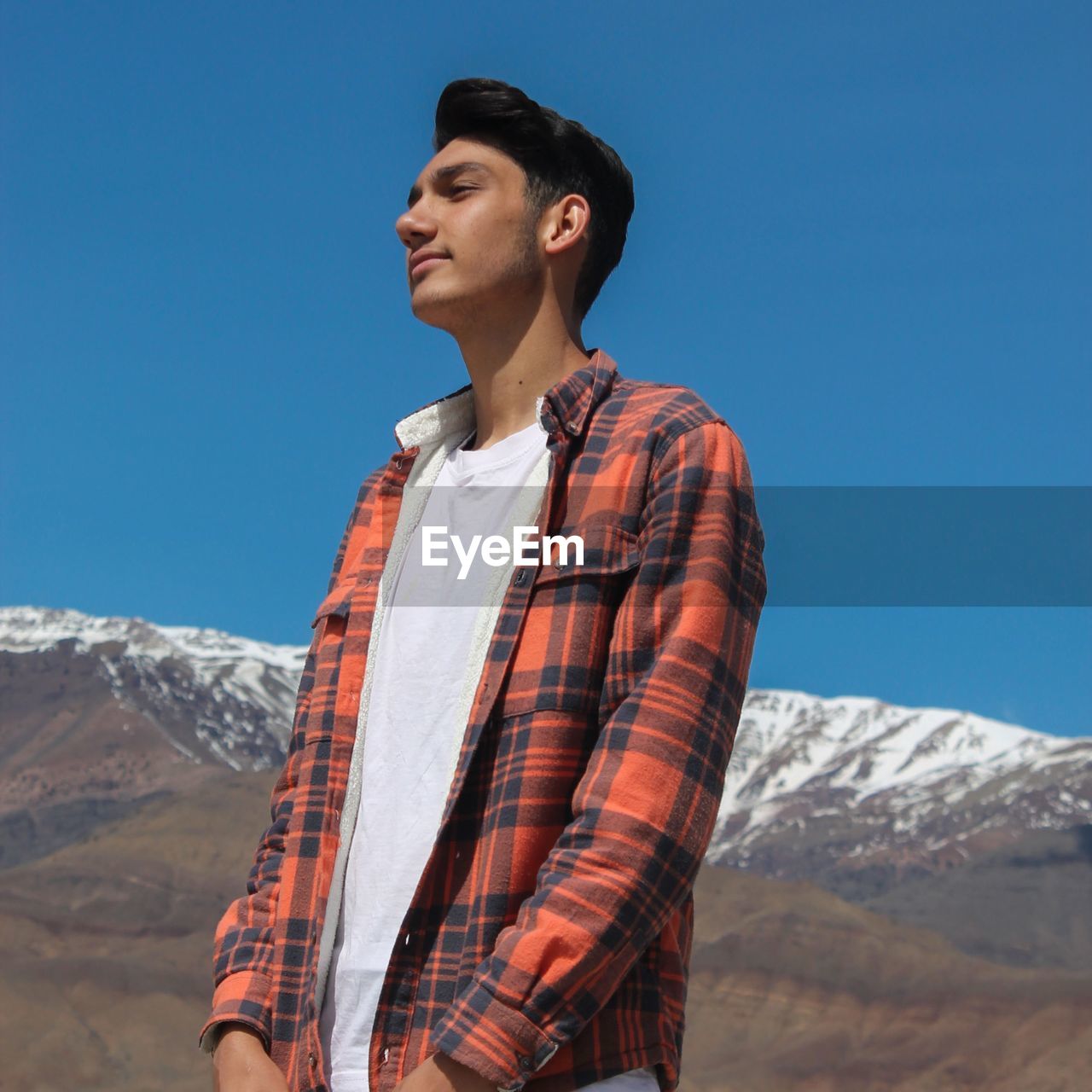 Young man standing on mountain against clear blue sky