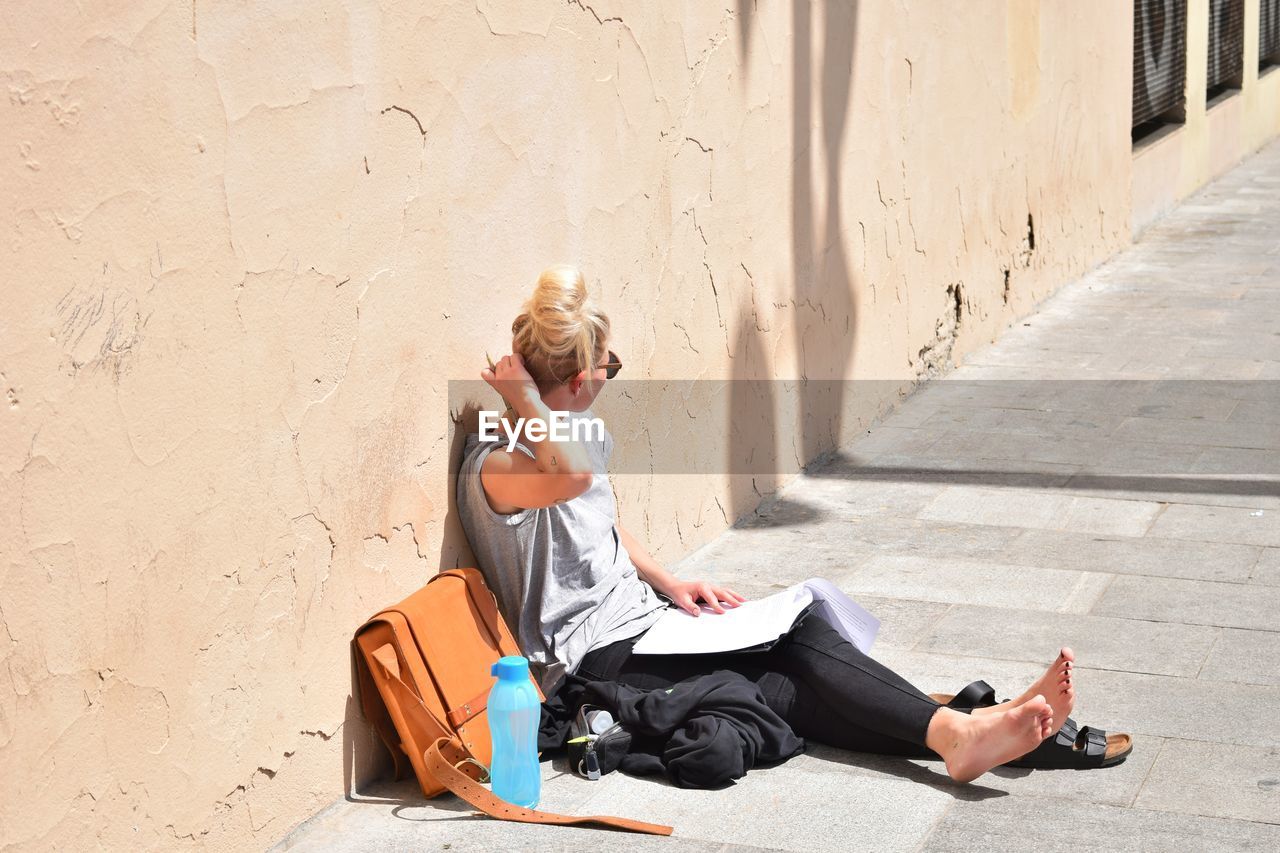 Young woman sitting against wall