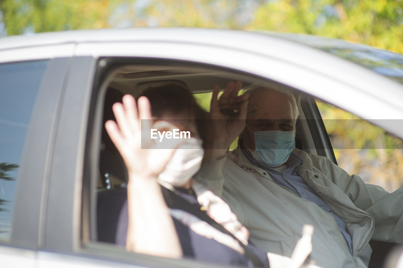Senior couple wearing anti virus masks are driving in a car during the covid-19 pandemic