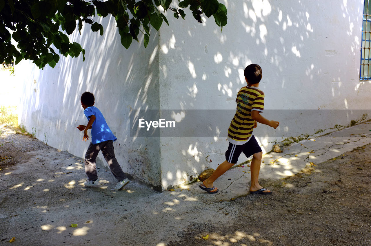 Boys running on footpath by house wall