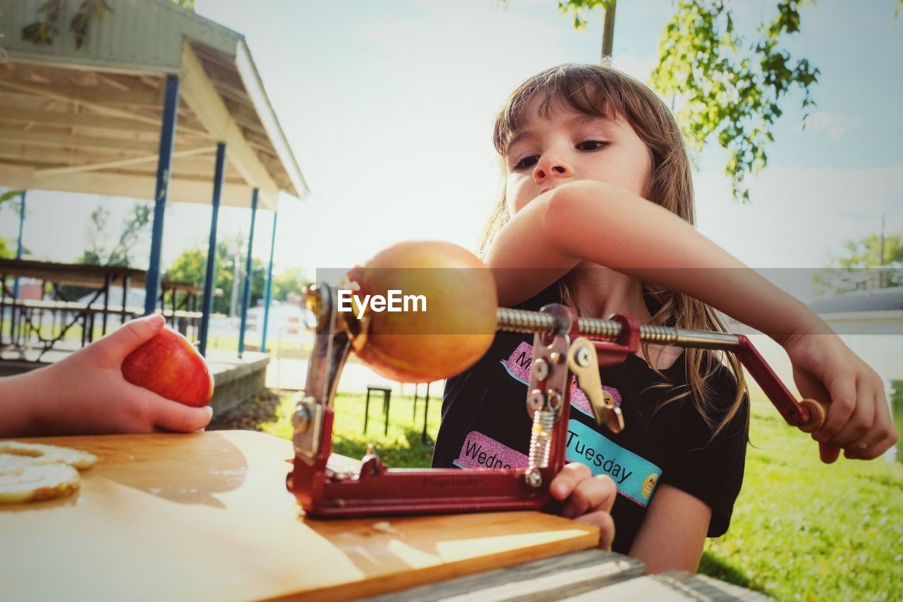 Cute girl holding fruit peeler on table outdoors