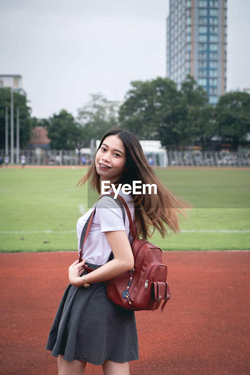 Portrait of young woman wearing backpack while standing on running track