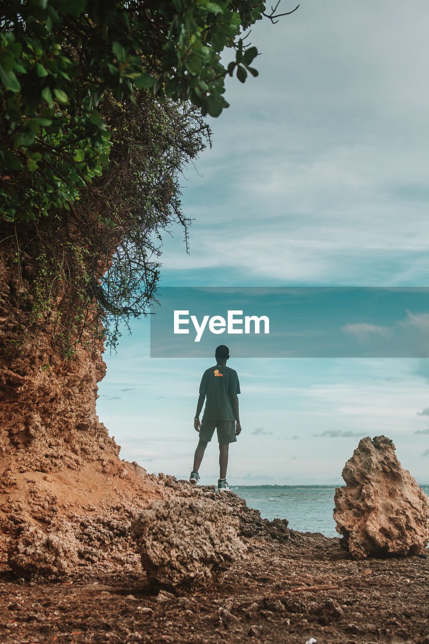 Young adult standing on the edge of a rock object against ocean