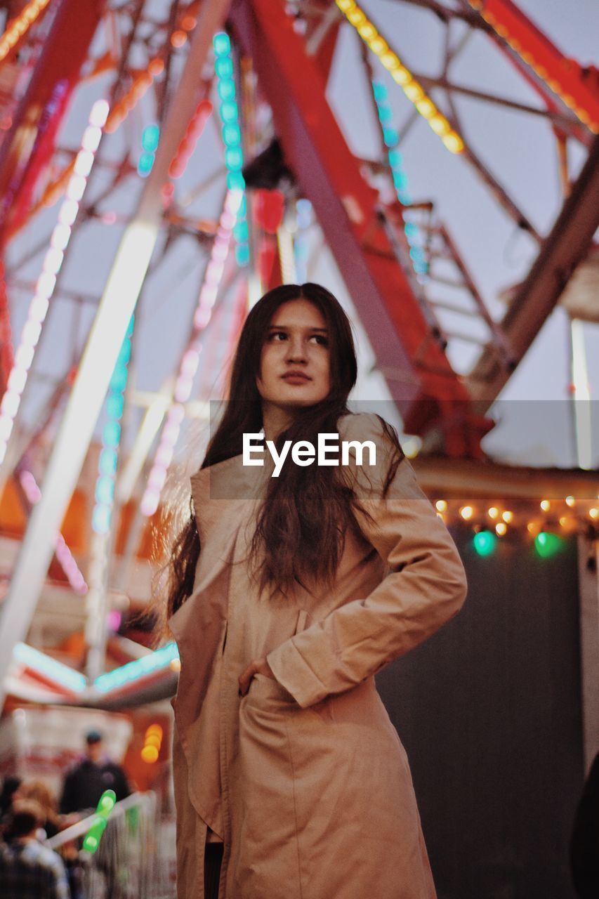 Low angle view of beautiful woman standing against illuminated ferris wheel