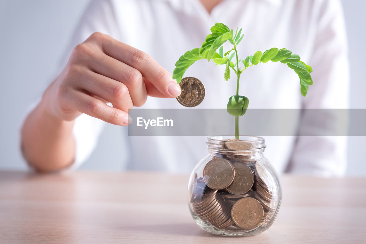 midsection of person putting coin in jar on table