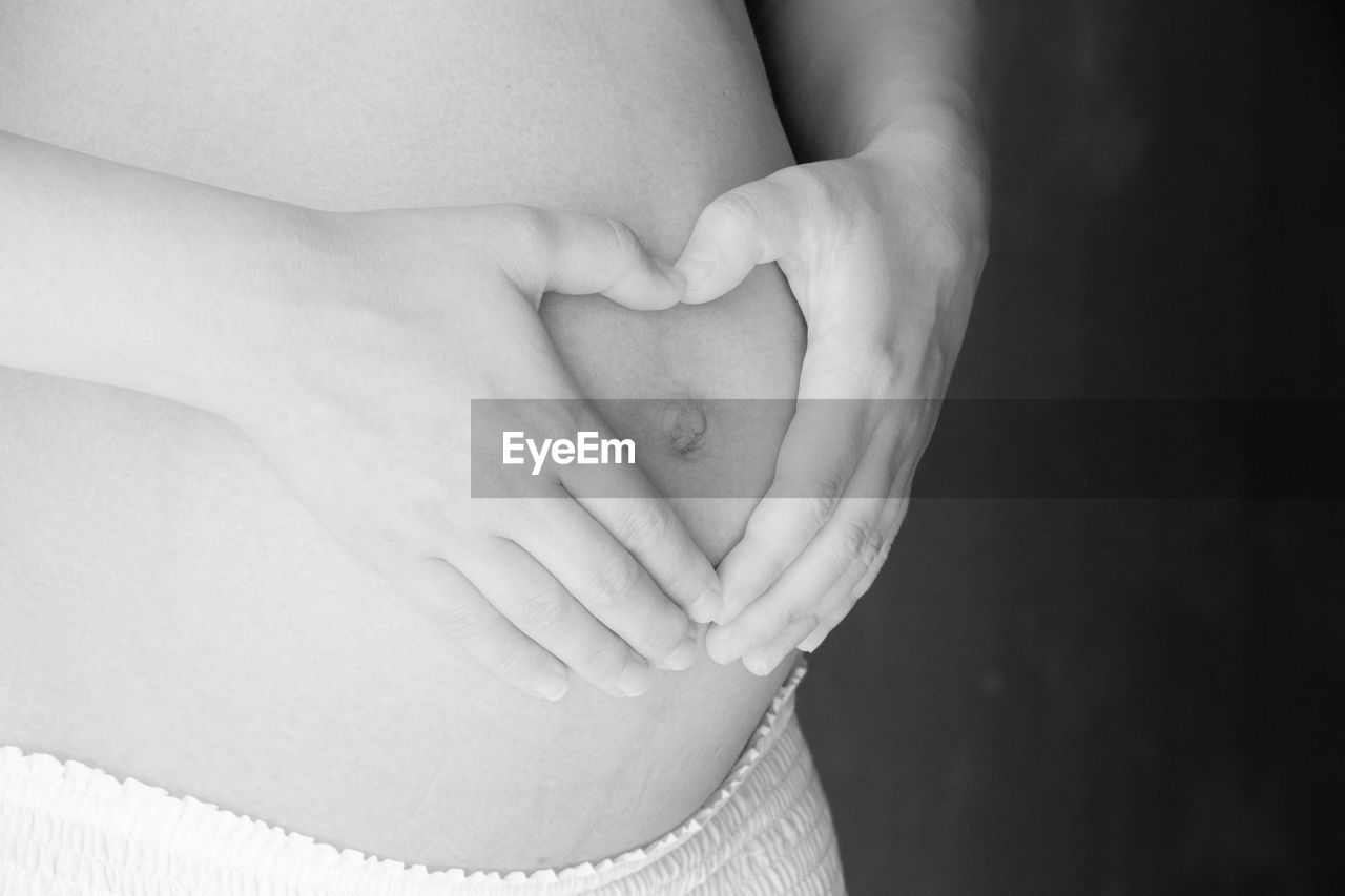 Midsection of pregnant woman making heart shape with hands on stomach