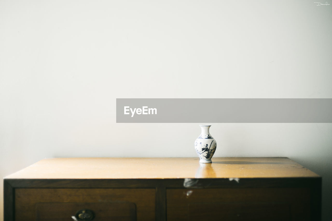 Vase on wooden table against wall at home