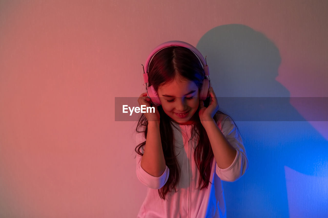 Beautiful happy little girl in headphones listening to music in neon light