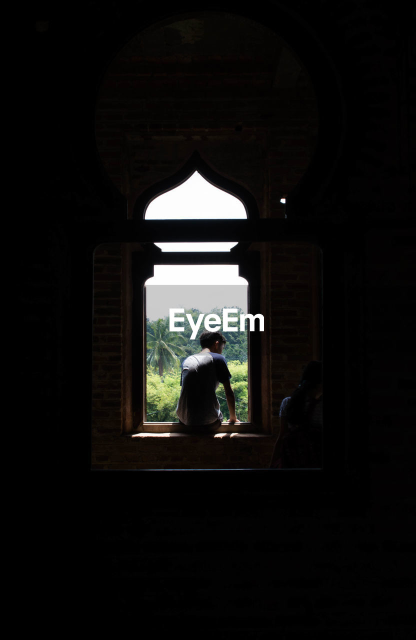 SILHOUETTE OF WOMAN LOOKING THROUGH WINDOW AT ARCHWAY