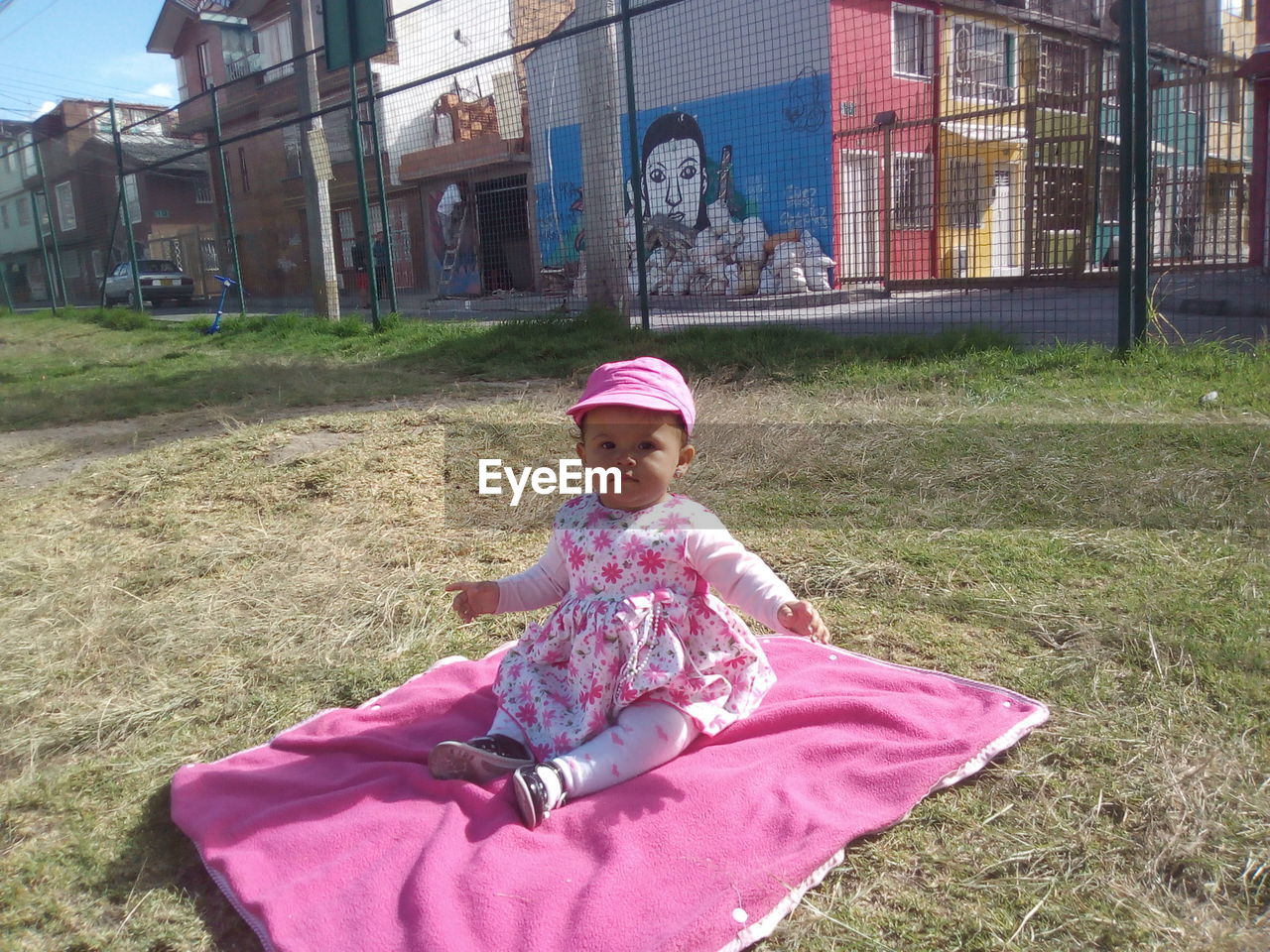 GIRL SITTING ON GRASS AGAINST WALL