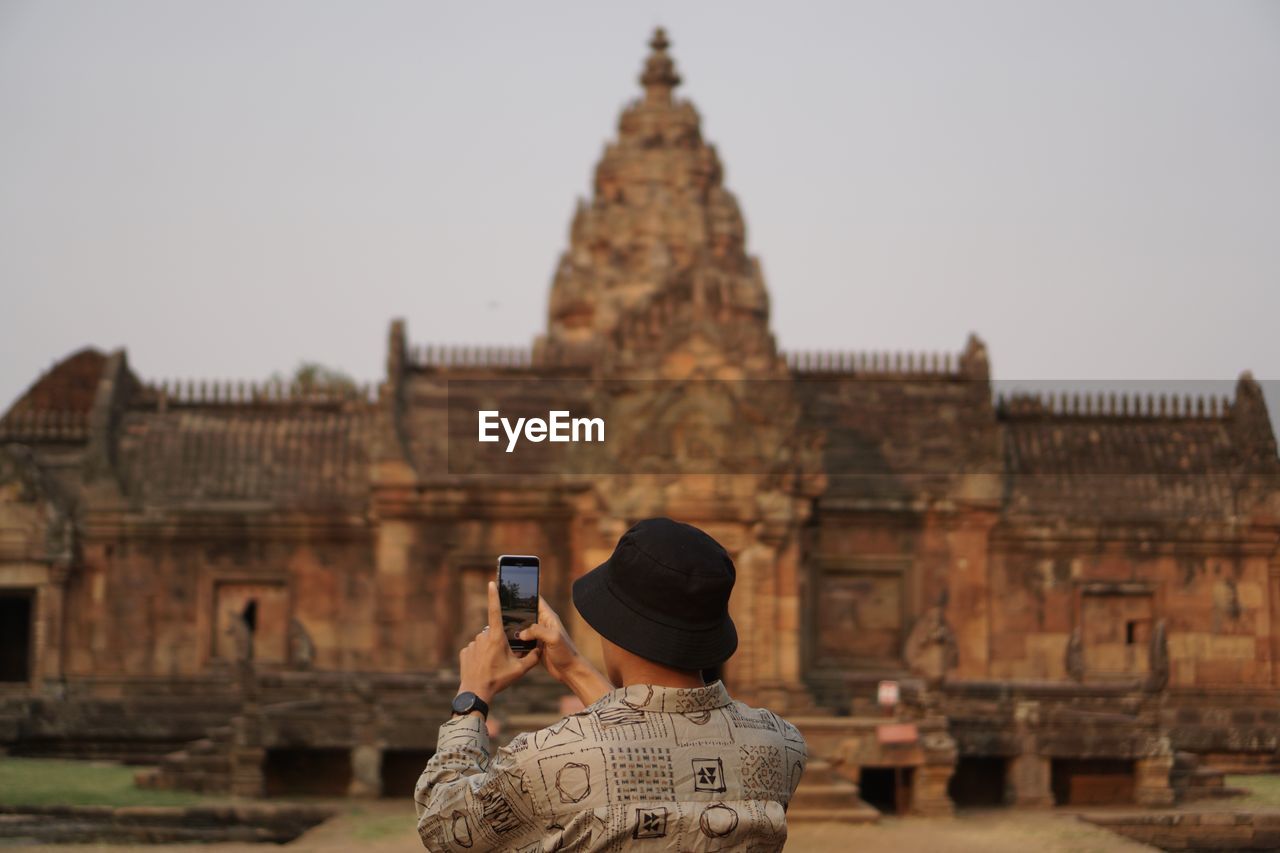 Man photographing with mobile phone against sky