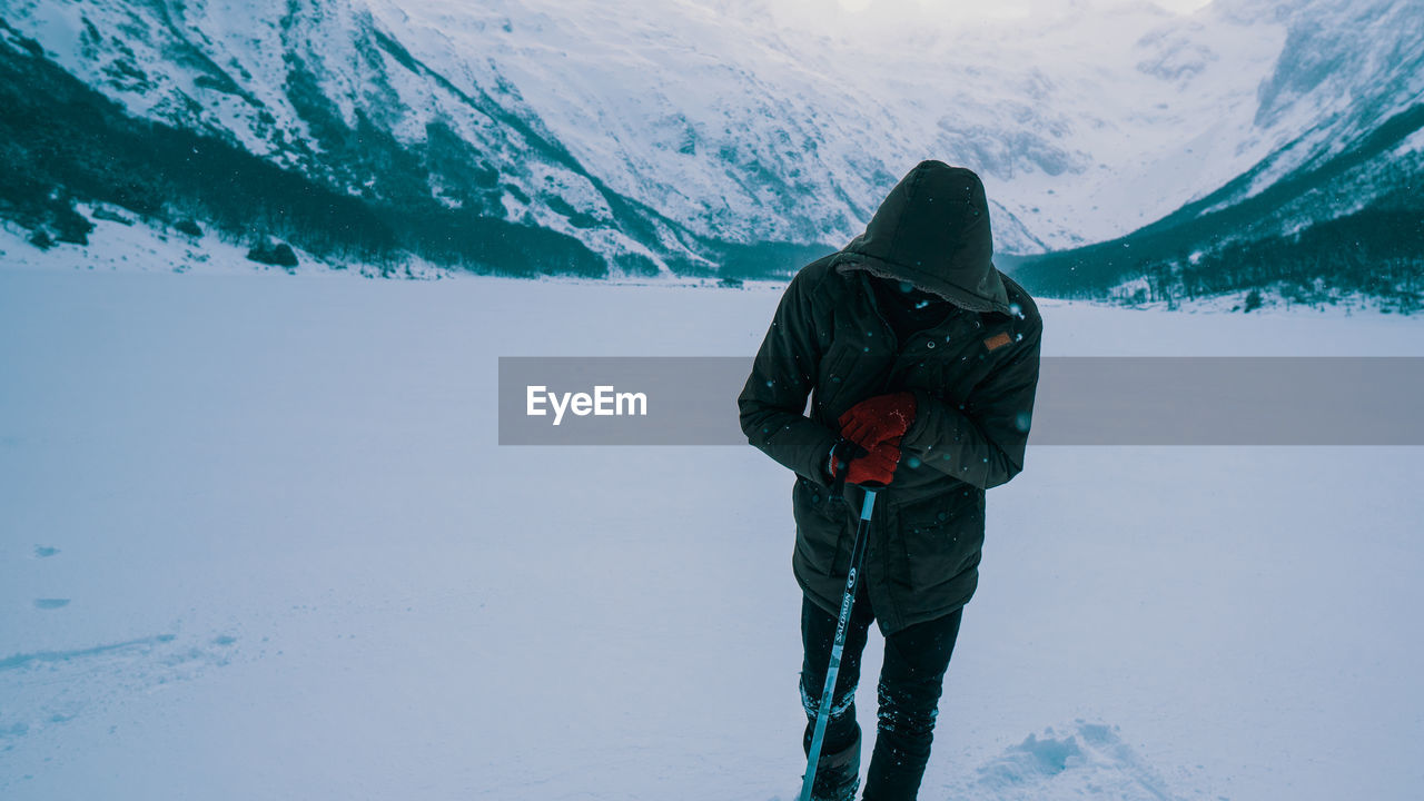 Man with hiking pole standing on snow covered mountain