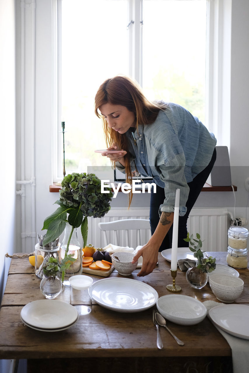 Woman photographing plates and food on table at home