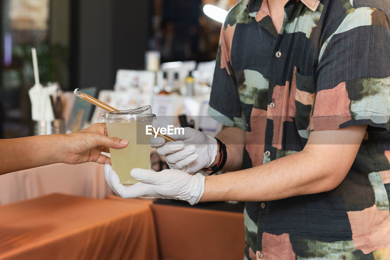 Man barista wearing groves serving drink to customer in cafe