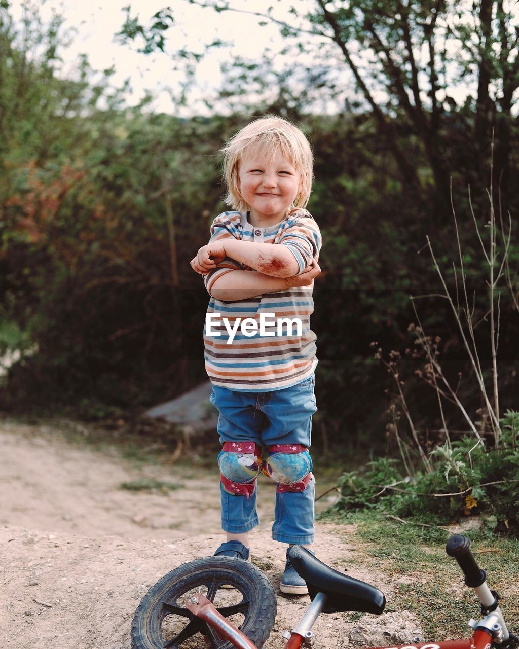 Portrait of crying boy showing injured elbow while standing by bicycle