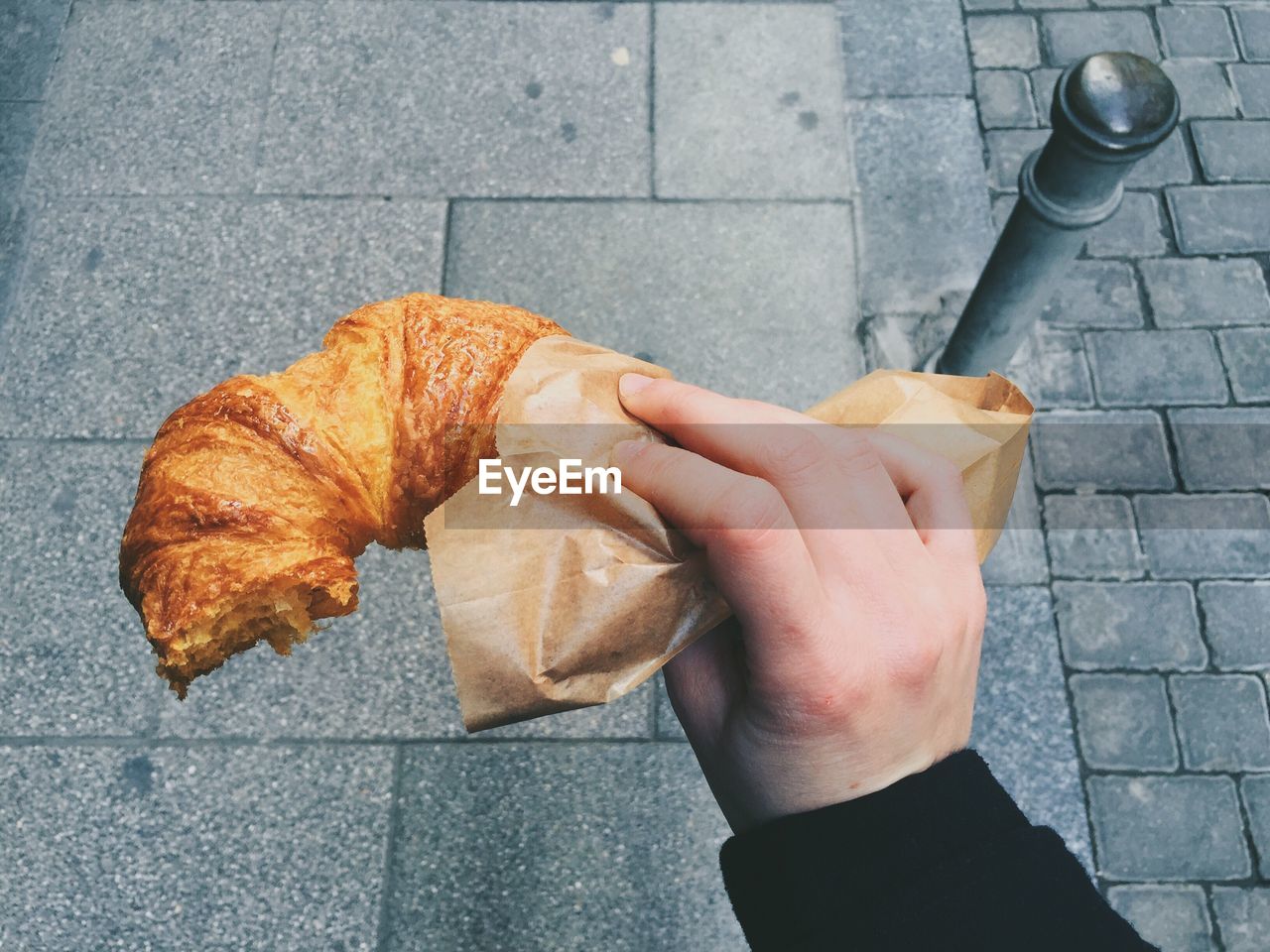 Cropped image of hand holding croissant on footpath