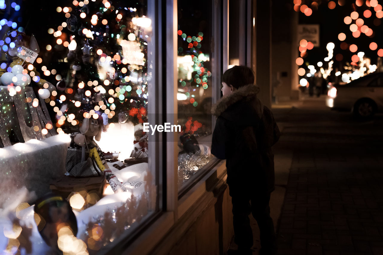 Small young boy looking at christmas decorations inside a store window