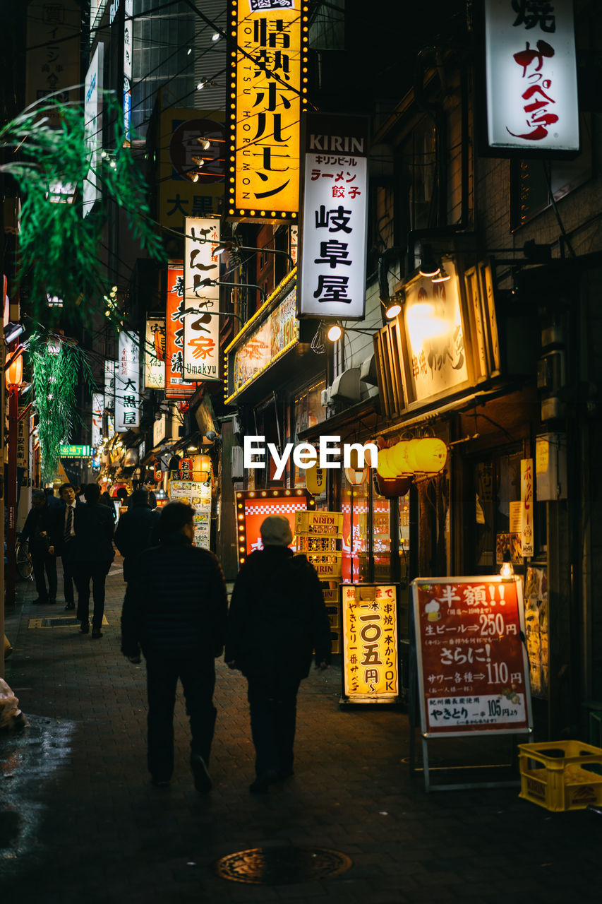 PEOPLE WALKING ON ILLUMINATED STREET AT NIGHT