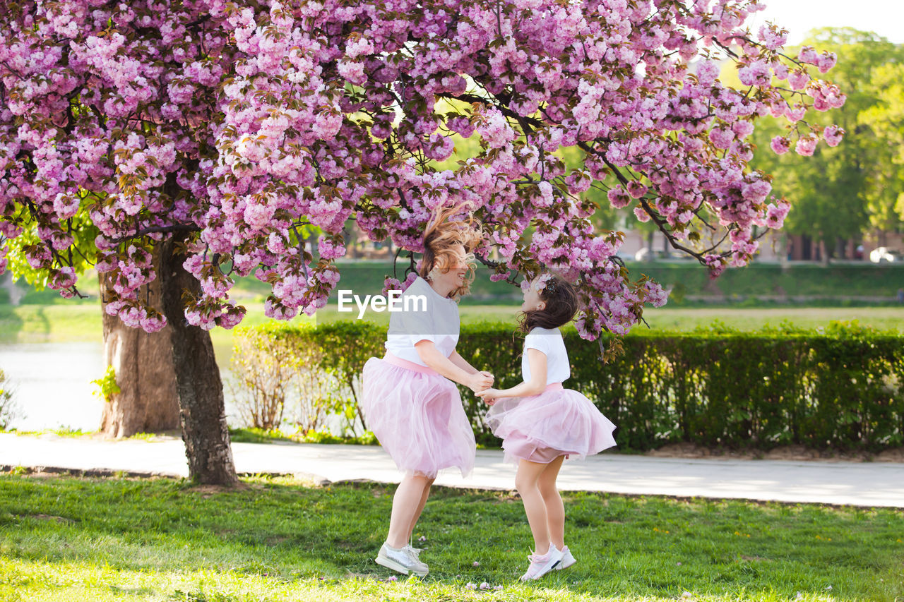 Full length of girls playing by flowering tree