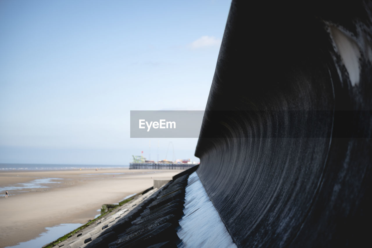 CLOSE-UP OF METALLIC STRUCTURE ON SEA SHORE AGAINST SKY