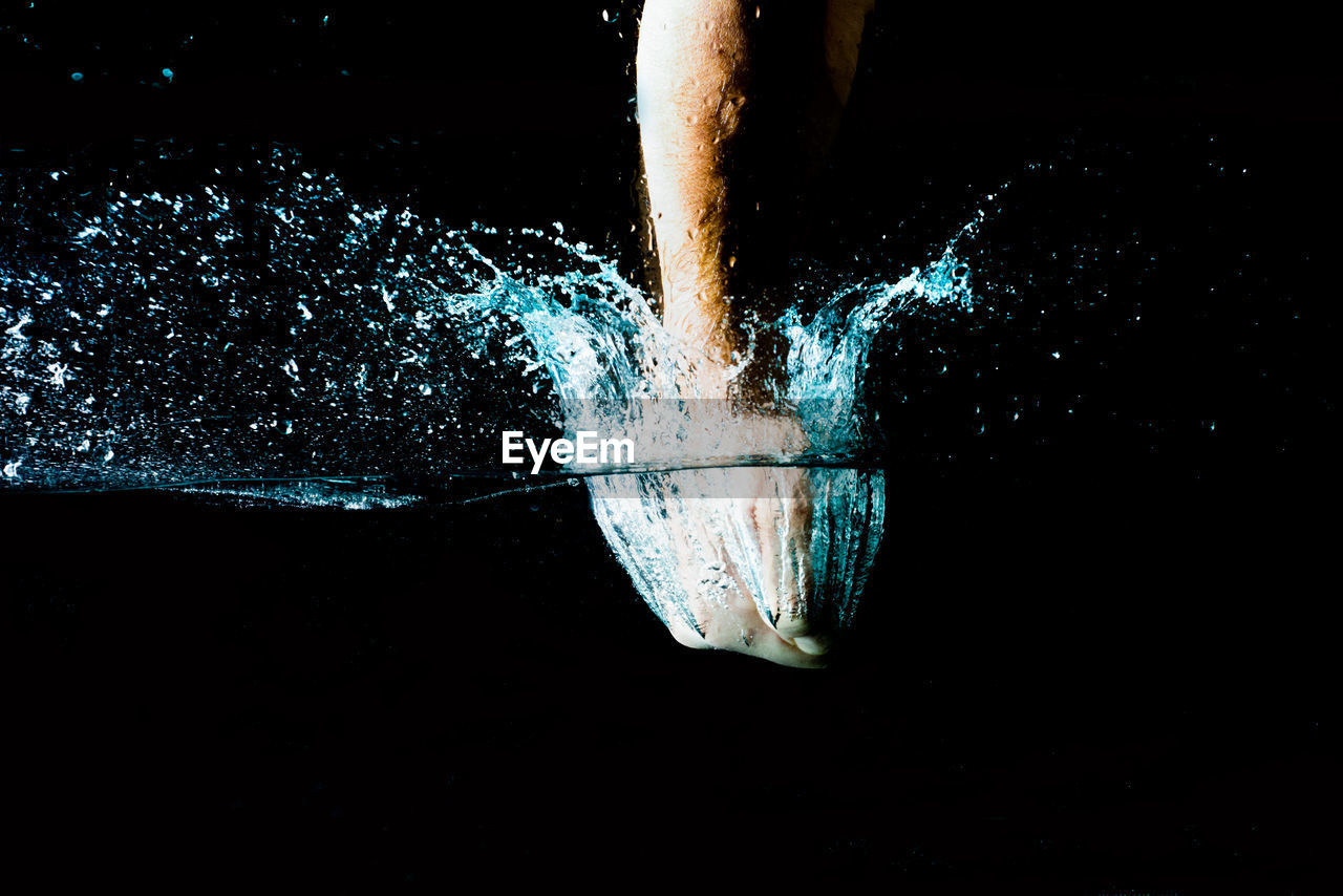 Human hand splashing water against black background